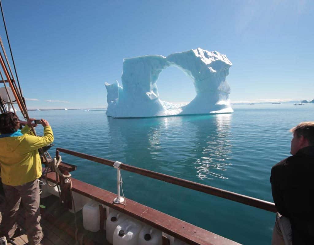 An arched iceberg against a blue sky, viewed from the deck of sailing ship. Enjoy polar sailing holidays with classic sailing.