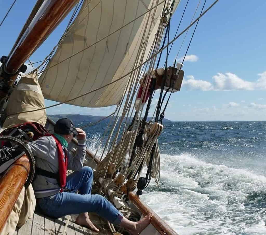 sailing aboard pilot cutter mascotte on a bright sunny day. the boat heels over and silver spray comes over the deck. Adventure holidays with classic sailing.
