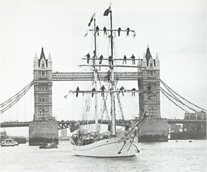 Old photograph of Eye of the Wind with crew on the yardarms and tower bridge in the background