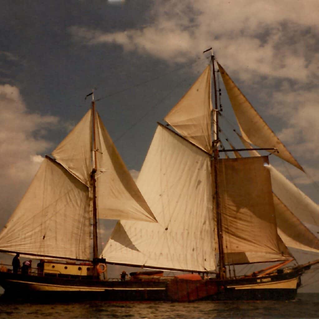 An old photograph of sail cargo ship De Tukker with golden light on the sails.