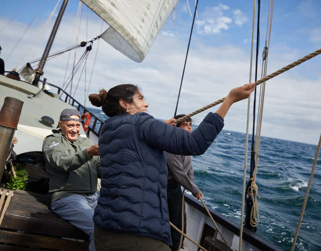 Two sailors hauling lines on the deck of Lugger Grayhound. You can learn the ropes with a sailing adventure through Classic Sailing.