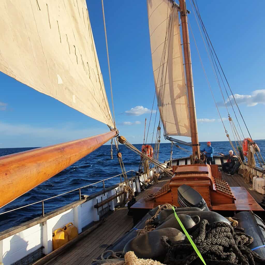 Looking aft along the deck of Leader under sail, in bright sunshine. Adventure holidays on the water with Classic Sailing.