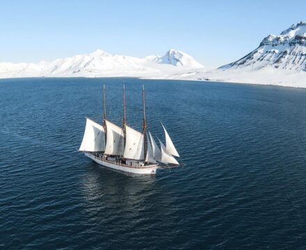 Linden on a sailing and scientific expedition in Svalbard. Sailing in the sunshine with a snowy landscape behind. Join her through Classic Sailing Photo Credit: Rasmus Djerf