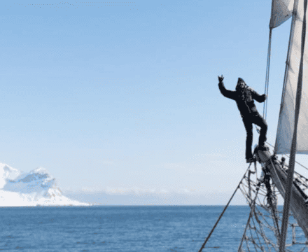 Happy crew member on the bowsprit of Linden, sailing on an expedition to Svalbard with Classic Sailing