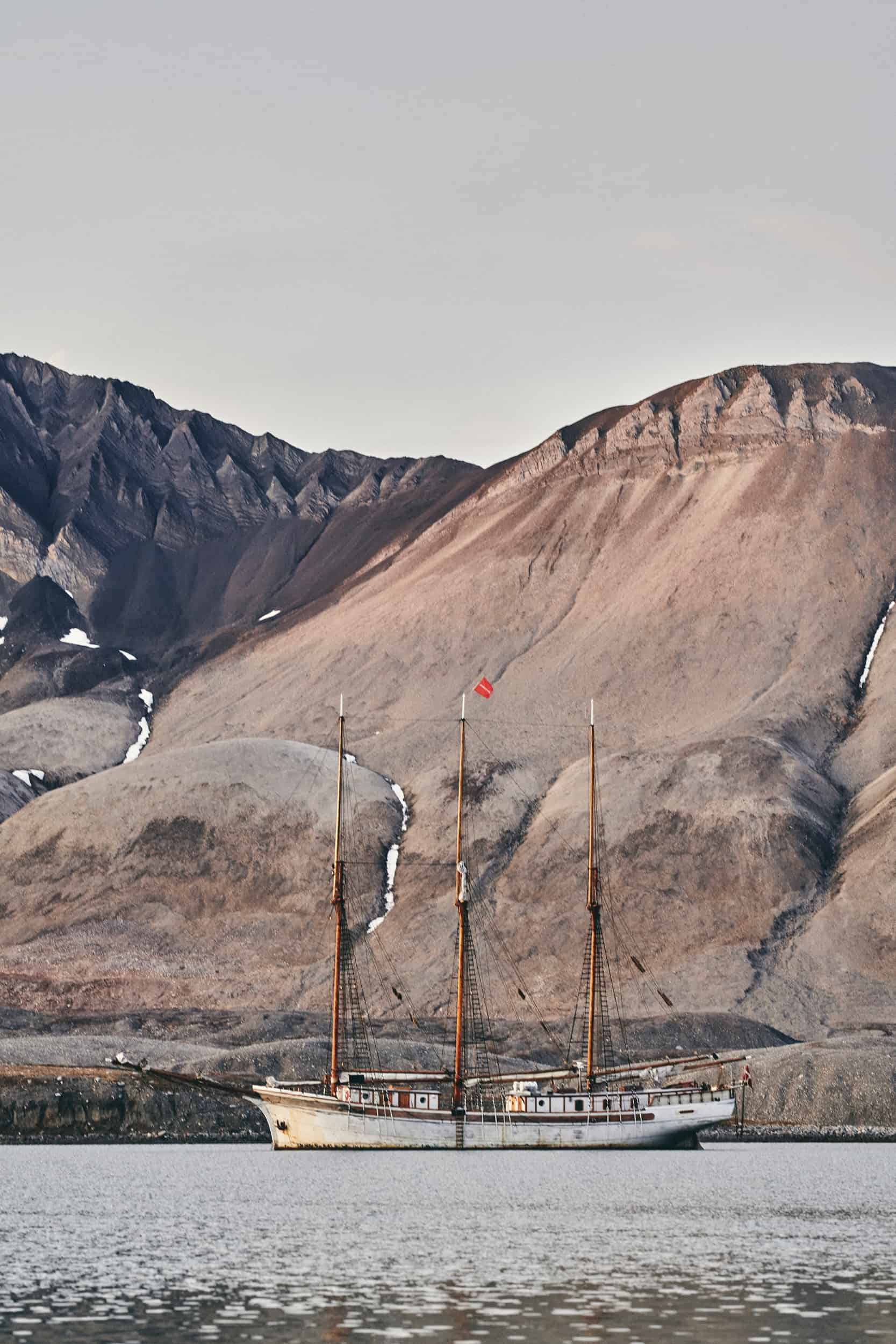 Sailing schooner in front of a rocky background on the shore of Svalbard. Fascinating geology and citizen science projects in the Arctic through Classic Sailing.